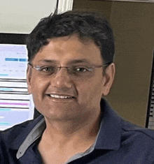 a man wearing glasses and a blue shirt is smiling and looking at the camera .