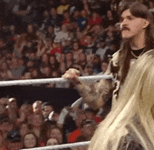 a man with long hair is standing in a wrestling ring .