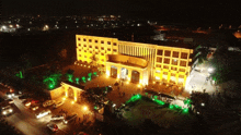 an aerial view of a large building lit up at night with cars parked in front of it