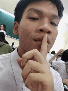 a young man holds his finger to his mouth in a classroom