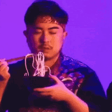 a man is eating noodles from a bowl with chopsticks while wearing a headband .