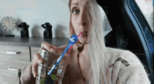 a woman is drinking a glass of water through a straw while sitting in a car .