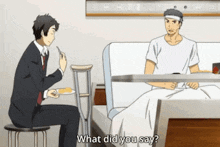 a man sitting at a table with a plate of food talking to another man in a hospital bed ..