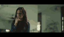 a woman in a blue shirt holds her hand to her mouth
