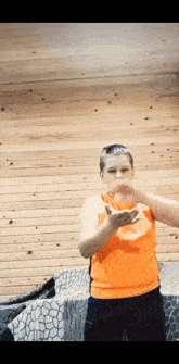 a young boy in an orange shirt is making a funny face while standing in front of a wooden wall