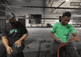 a man wearing a black shirt that says hip hop on it sits next to another man wearing a green shirt