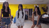 three women are dancing in front of a yellow wall with a start sign
