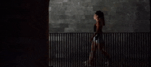 a woman is walking across a fence at night in front of a brick wall .