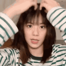 a woman in a green and white striped shirt is holding her hair .