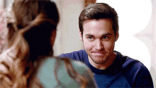 a man in a blue shirt is making a funny face while looking at a woman .