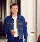 a man wearing a denim jacket and a white shirt is standing in a doorway .