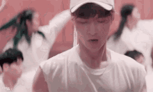 a young man wearing a baseball cap and a white shirt is standing in front of a group of people .