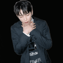 a man in a suit holds his hands to his chest in front of a black background