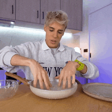 a man wearing a new york sweatshirt is mixing something in a bowl