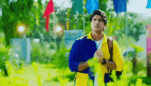 a man in a blue and yellow jacket is standing in a park with flags in the background .