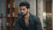 a man with a beard is sitting at a table in a living room .