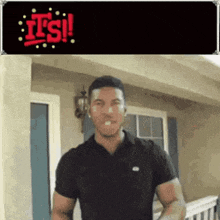 a man in a black shirt is standing in front of a house with the words it 's !