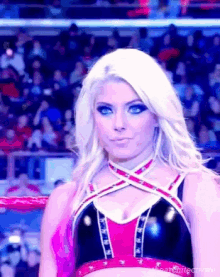 a woman in a wrestling outfit is standing in a ring with a crowd behind her .