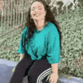 a woman is sitting on a bench wearing a blue shirt and black pants .
