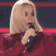 a blonde woman in a red dress is singing into a microphone .
