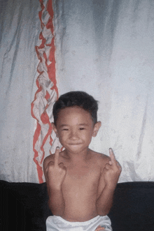 a shirtless child giving the middle finger in front of a white curtain