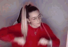 a woman wearing glasses and a red sweater is dancing in front of a computer .