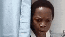 a young boy is peeking out from behind a shower curtain in a bathroom and making a funny face .