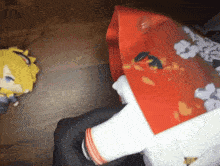 a person is holding a red and white bag with flowers on it and a stuffed animal in the background