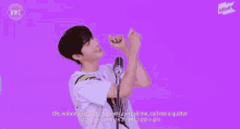 a young man is standing in front of a microphone with his hands in the air and singing into it .