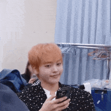 a young man with orange hair is holding a cell phone in his hand