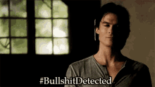 a man in a gray shirt says #bullshitdetected in front of a window