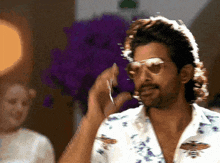 a man wearing sunglasses and a floral shirt is smiling
