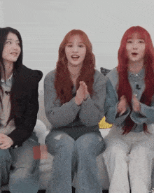 three girls with red hair are sitting on a couch clapping