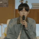a man in a denim jacket is holding a microphone in his hand
