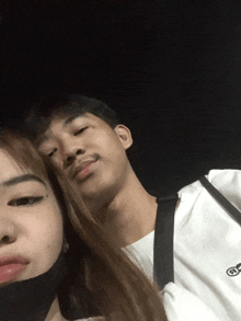 a man and a woman are posing for a picture and the man is wearing a white shirt with the letter s on the front
