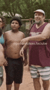 a man in a maroon tank top is standing next to a boy in striped shorts