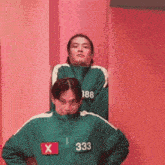 a man in a green jacket with the number 333 on it stands next to another man .