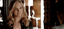 a woman wearing a necklace and a black jacket is smiling at a man .