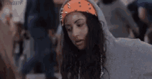 a woman wearing a hoodie and an orange bandana is standing in a crowd of people .