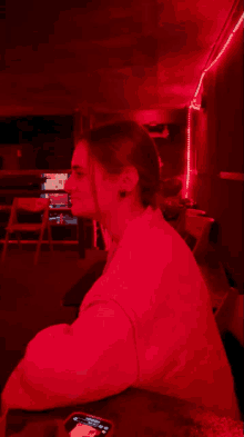 a woman sits at a table in a dark room with a red light behind her