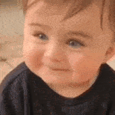 a baby with blue eyes is smiling and looking at the camera while wearing a black shirt .