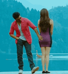 a man in a pink jacket is touching a woman 's butt while standing next to a body of water .