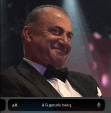 a man in a tuxedo and bow tie is smiling while sitting in front of a microphone .