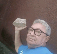 a man wearing glasses is holding a rock in his hand .