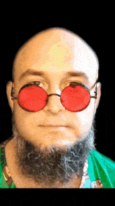 a bald man with a beard wears red sunglasses