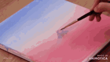 a person is painting a pink and blue sunset on a canvas .