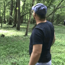 a man in a black shirt and blue hat is throwing a frisbee in the woods