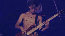 a man without a shirt is playing a guitar with the letter d visible in the corner
