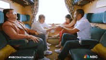 a group of people are sitting on a train with the nbc logo on the bottom left