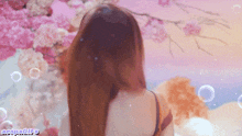 a woman with long hair stands in front of a wall of pink flowers and bubbles